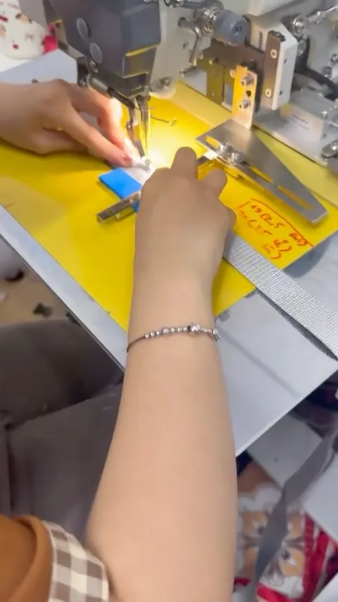 A seamstress' hands guiding webbing under an industrial sewing machine
