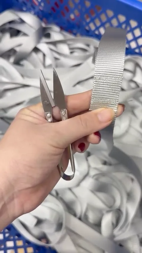 Hand holding thread snippers and a length of webbing at the QC table